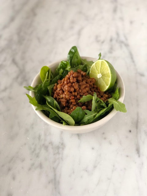 Load image into Gallery viewer, A delicious bowl of Peruvian Lentils Sofrito with lime over spinach leaves. 
