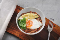 Load image into Gallery viewer, A bowl of Fillo&#39;s beans topped with egg, avocado, and garnish. 
